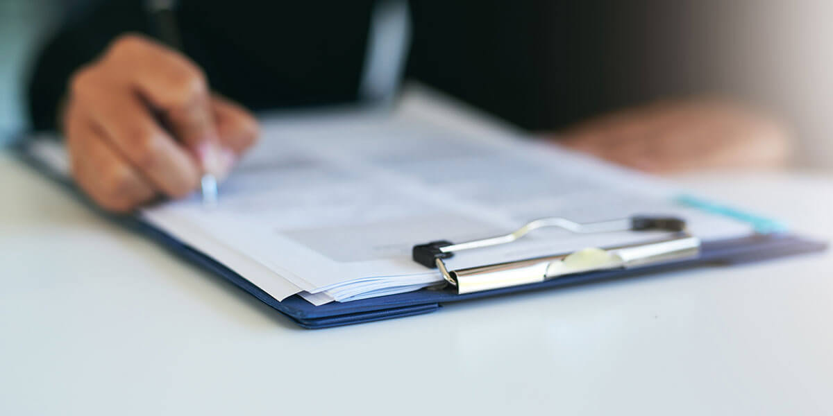 Person filling out paperwork on clipboard