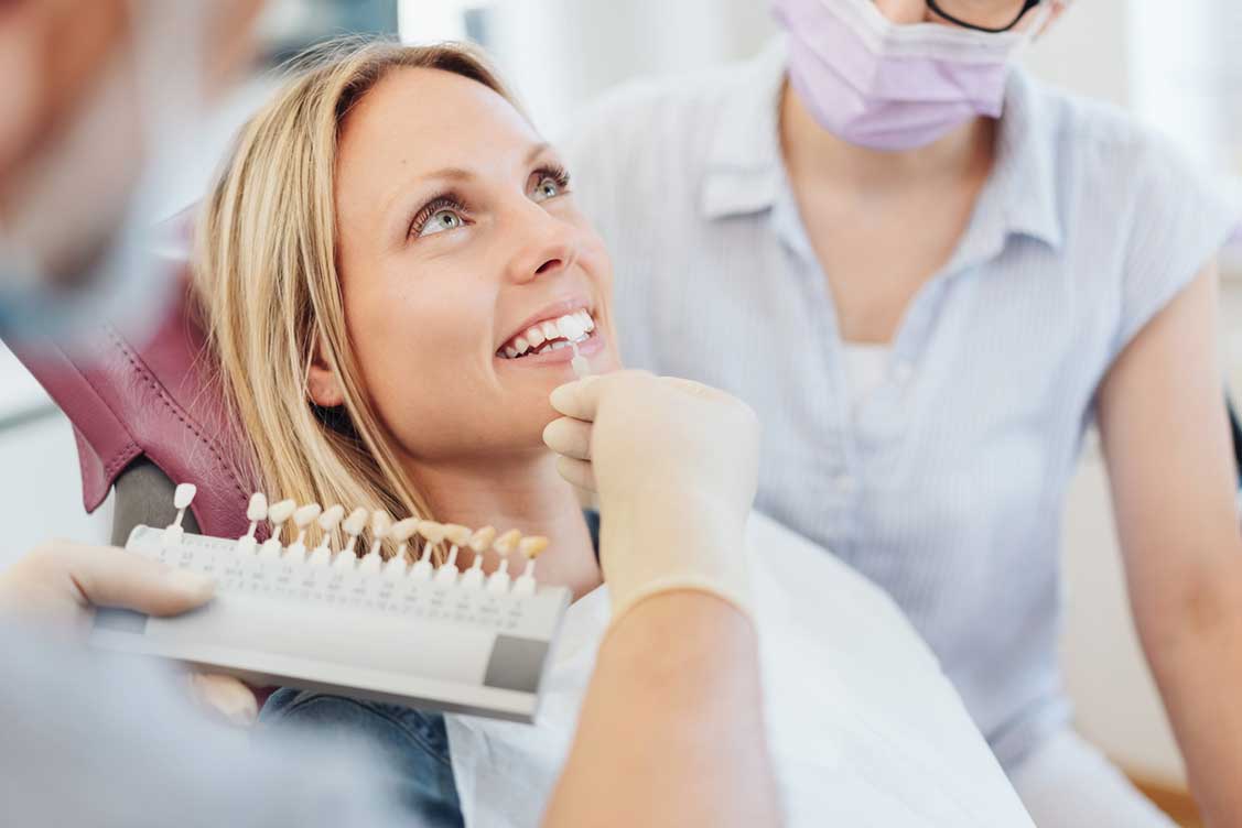 Dentist checking shade chart for woman’s veneers