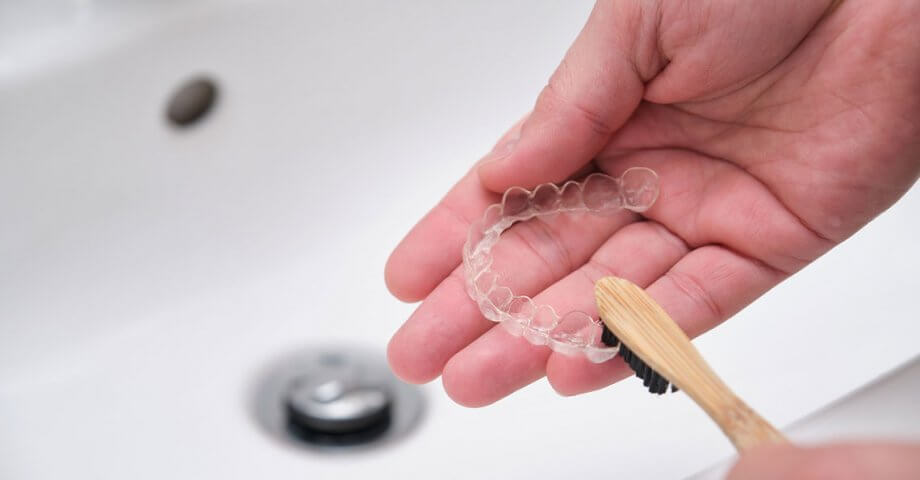 Hands cleaning clear aligners with toothbrush at sink